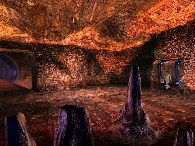 Inside a cave-like interior with rocky formations recalling another planet, a person in a coat steps through the right doorway. Its like theyve entered the heart of The Ward sci-fi adventure on Microsoft Windows PC CD.